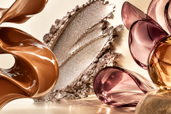 Abstract caramel lacquer ribbon, silver shimmer and plum glass shapes on a warm ivory background.